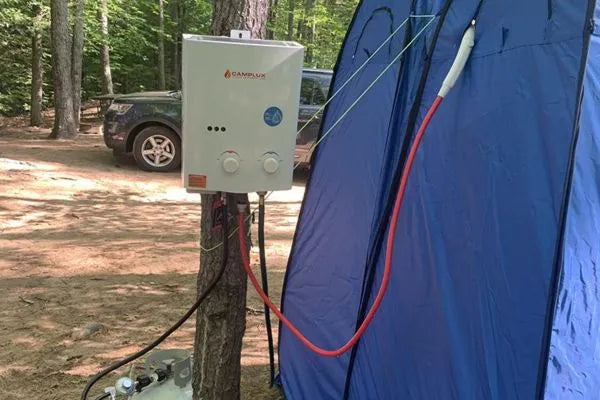 A Camplux portable water heater hanging on a tree